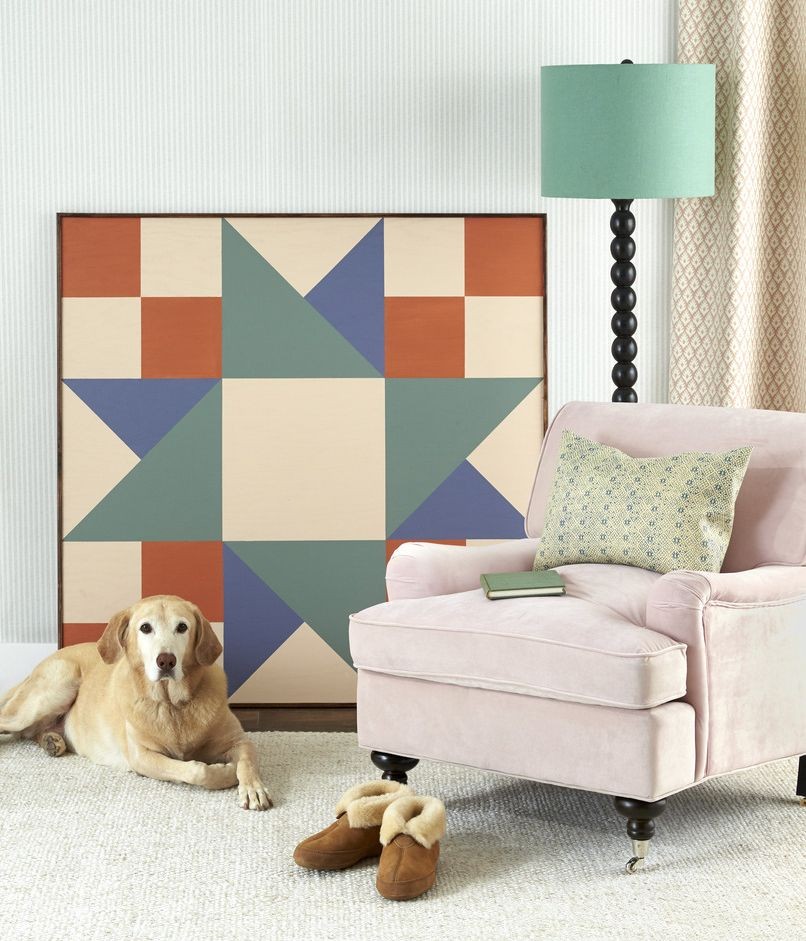 o piesa de arta mare, intr-o forma geometrica patrata, sprijinita pe un perete de o lampa de scaun si de un caine